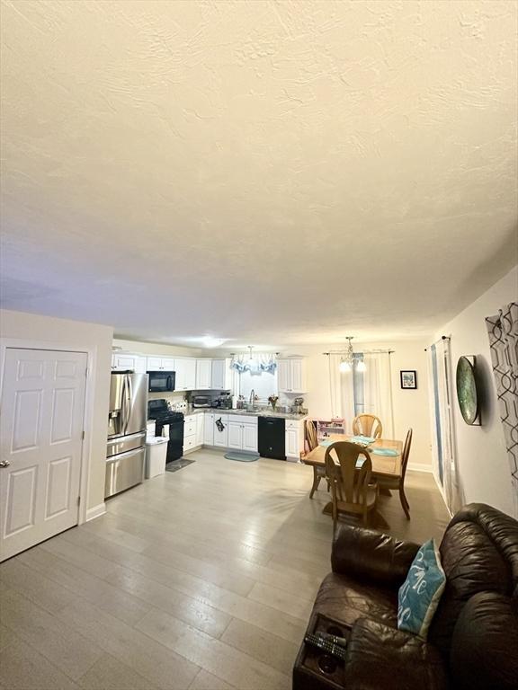 unfurnished living room with a sink, a textured ceiling, baseboards, and wood finished floors