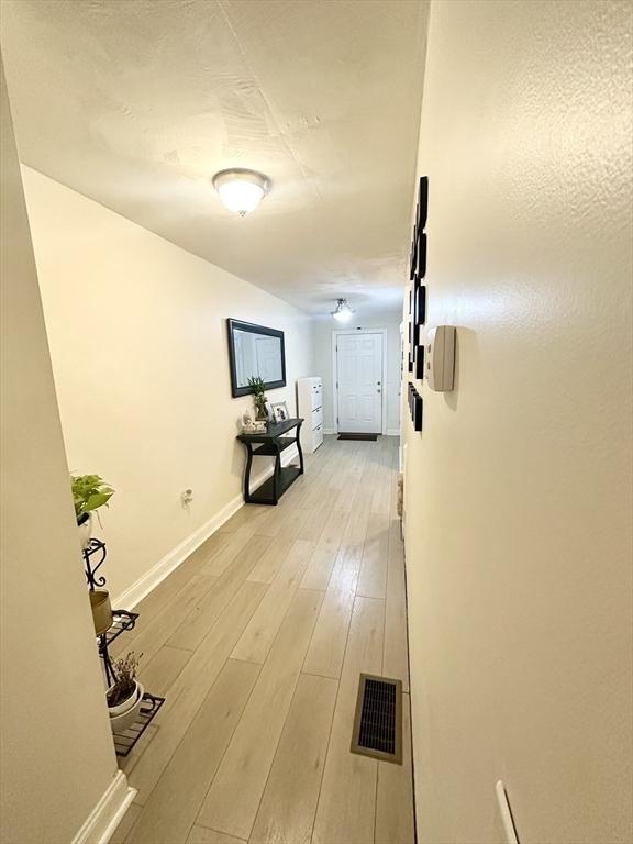 hallway with visible vents, baseboards, and light wood finished floors