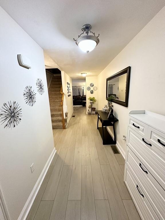 hall with stairs, visible vents, baseboards, and light wood finished floors