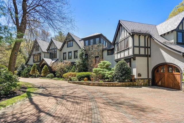 view of side of property featuring stone siding, stucco siding, and decorative driveway