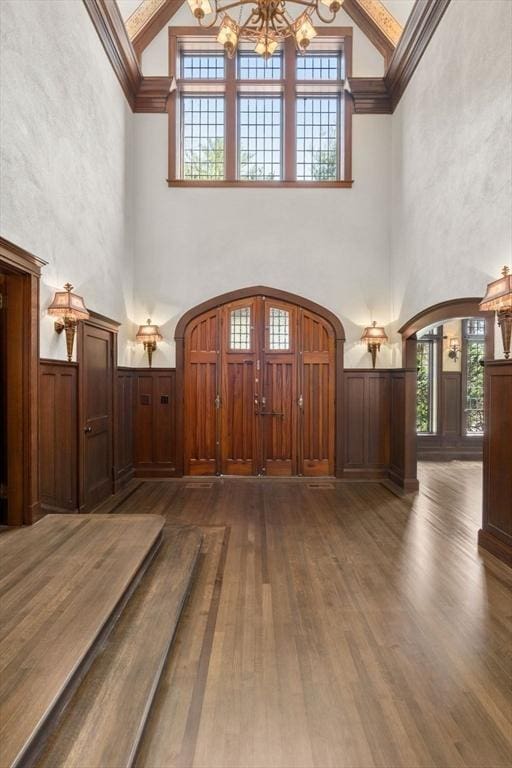 foyer entrance featuring a chandelier, arched walkways, high vaulted ceiling, healthy amount of natural light, and wood finished floors