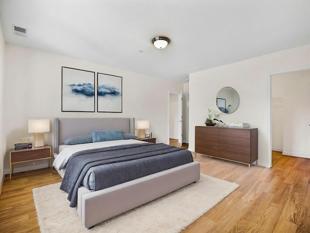 bedroom with baseboards, light wood finished floors, and visible vents