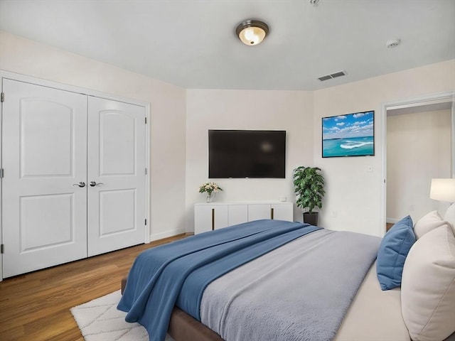 bedroom featuring baseboards, a closet, wood finished floors, and visible vents