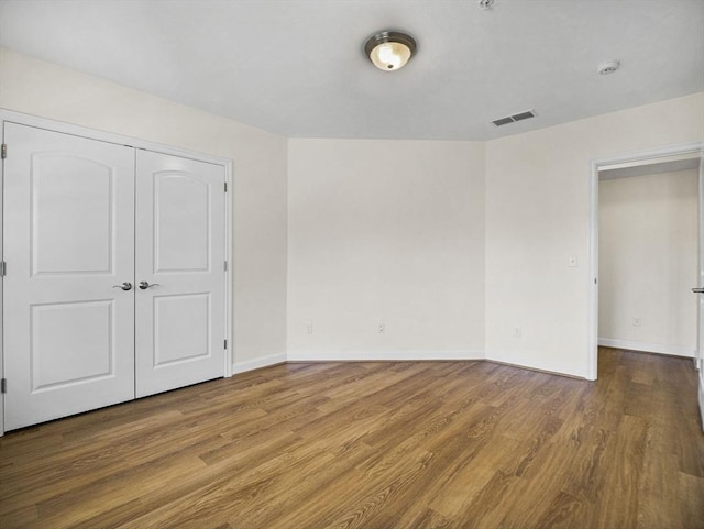 unfurnished bedroom featuring visible vents, baseboards, wood finished floors, and a closet
