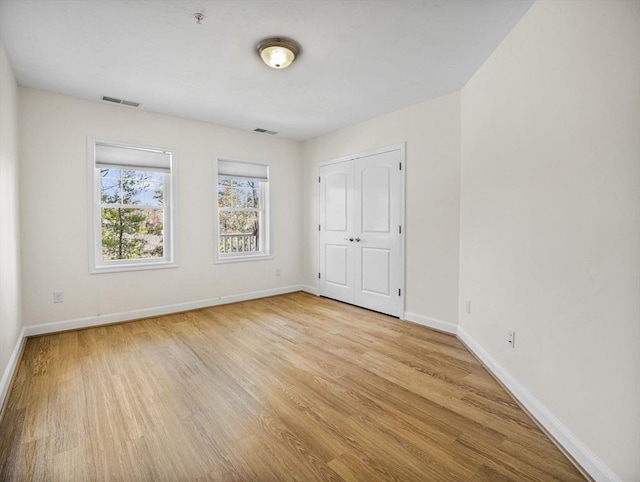 unfurnished bedroom featuring baseboards, a closet, wood finished floors, and visible vents