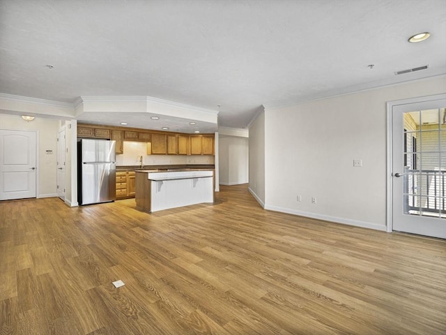 kitchen featuring brown cabinets, freestanding refrigerator, open floor plan, baseboards, and ornamental molding