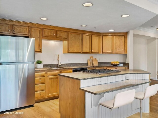 kitchen featuring stainless steel appliances, a kitchen breakfast bar, a sink, and light wood finished floors