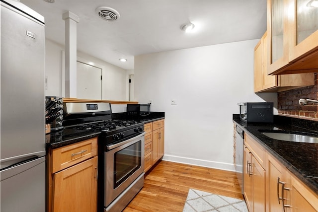 kitchen with sink, stainless steel appliances, tasteful backsplash, light hardwood / wood-style flooring, and dark stone counters