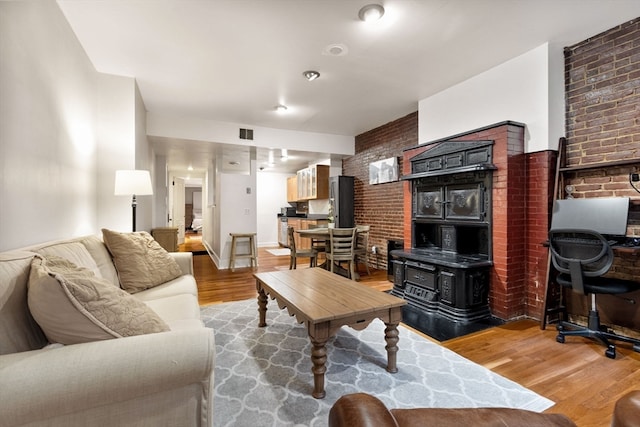 living room with a wood stove, hardwood / wood-style floors, and brick wall