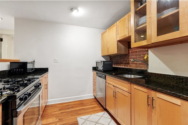 kitchen featuring light wood-type flooring, backsplash, stainless steel appliances, sink, and dark stone countertops