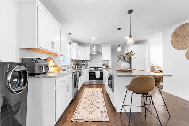 kitchen featuring white cabinets, wall chimney range hood, light stone countertops, a kitchen island, and stainless steel appliances