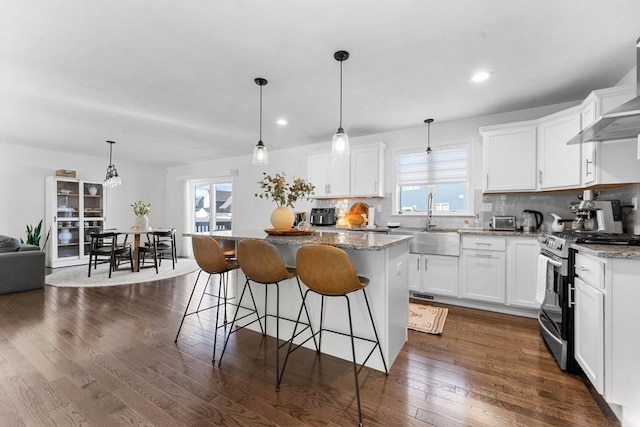 kitchen with a center island, hanging light fixtures, stainless steel stove, tasteful backsplash, and white cabinetry