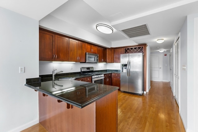 kitchen featuring light hardwood / wood-style flooring, appliances with stainless steel finishes, a kitchen bar, kitchen peninsula, and sink