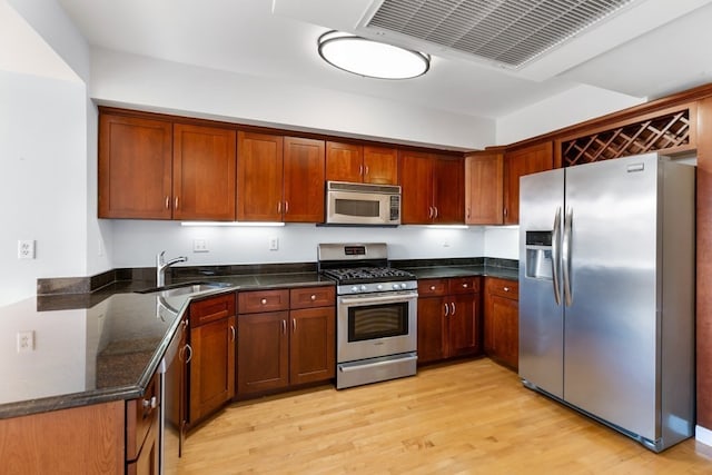 kitchen with dark stone countertops, sink, appliances with stainless steel finishes, and light hardwood / wood-style floors