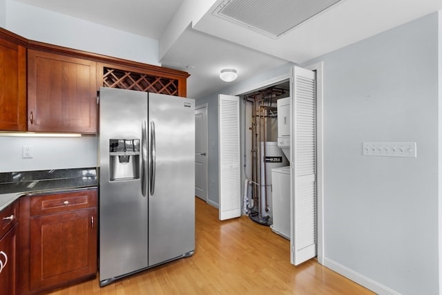 kitchen featuring light hardwood / wood-style flooring, dark stone countertops, stacked washer and dryer, and stainless steel fridge with ice dispenser