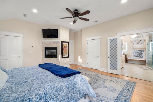 bedroom with ensuite bath, ceiling fan, a fireplace, light hardwood / wood-style floors, and vaulted ceiling