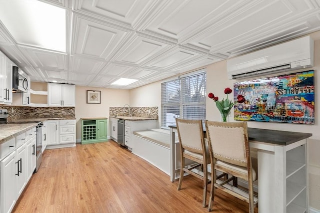 kitchen with an AC wall unit, tasteful backsplash, white cabinets, light hardwood / wood-style floors, and stainless steel appliances