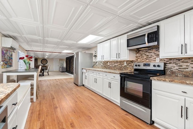 kitchen with appliances with stainless steel finishes, tasteful backsplash, a wall mounted AC, white cabinets, and light hardwood / wood-style floors