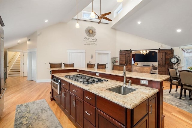 kitchen featuring pendant lighting, stainless steel gas stovetop, sink, a kitchen island with sink, and a barn door