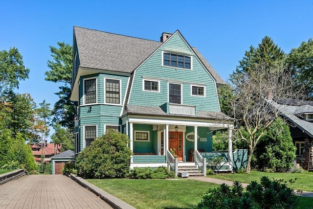 victorian house featuring a shingled roof, covered porch, a front lawn, and a chimney