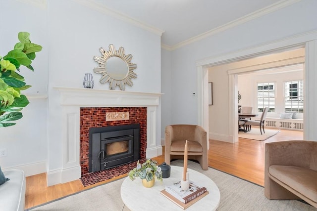 living area featuring crown molding, a brick fireplace, wood finished floors, and baseboards