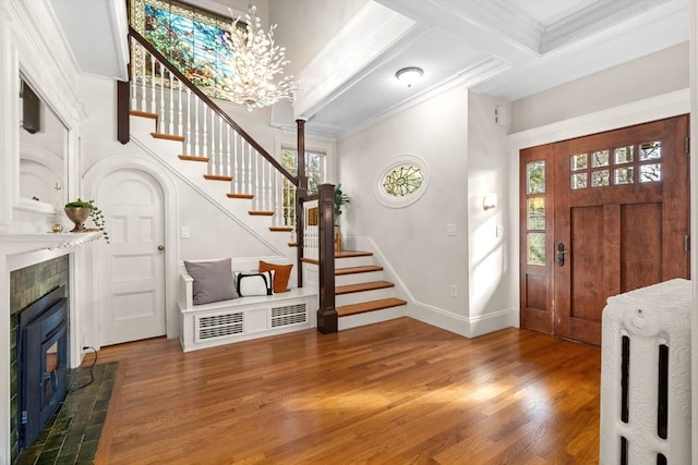 entryway featuring wood finished floors, a tiled fireplace, ornamental molding, and stairs