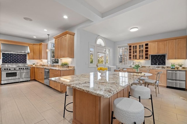 kitchen with open shelves, wall chimney exhaust hood, a breakfast bar, range with two ovens, and light stone counters