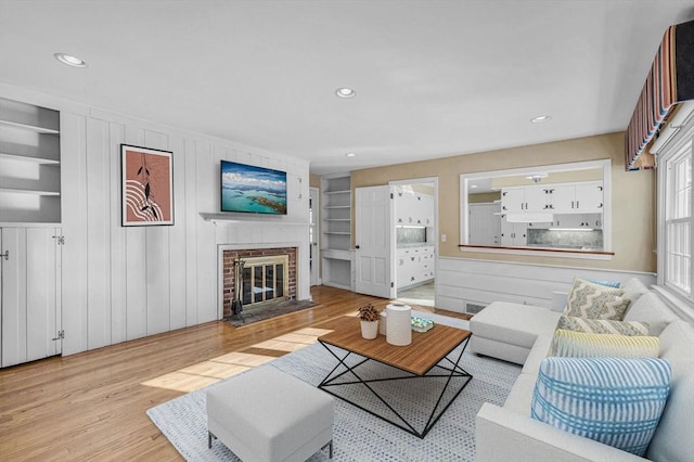 living area with built in shelves, recessed lighting, a fireplace, and light wood-style floors