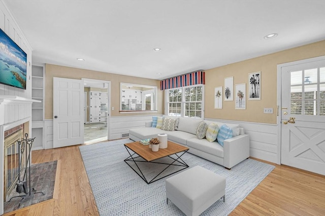 living area featuring a glass covered fireplace, a wainscoted wall, light wood-type flooring, built in shelves, and recessed lighting