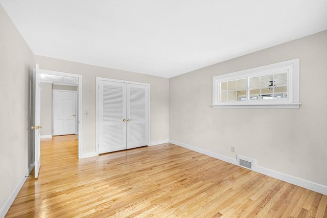 unfurnished bedroom featuring light wood-type flooring, baseboards, visible vents, and a closet