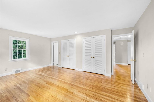 unfurnished bedroom featuring multiple closets, visible vents, light wood-style floors, and baseboards