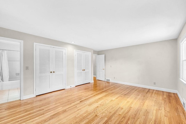 unfurnished bedroom featuring light wood finished floors, baseboards, two closets, and ensuite bathroom