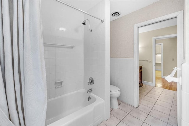 full bathroom with visible vents, toilet, tile patterned floors, shower / bath combo with shower curtain, and tile walls