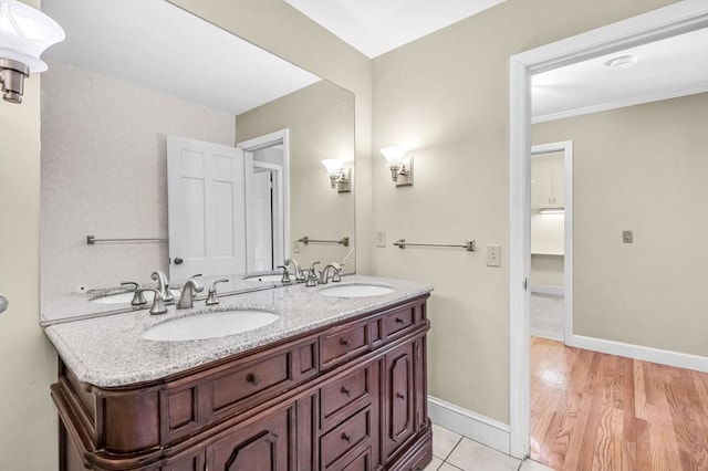 bathroom featuring wood finished floors, a sink, baseboards, and double vanity