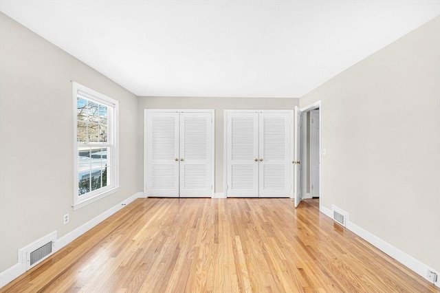 unfurnished bedroom with baseboards, light wood-style flooring, visible vents, and multiple closets