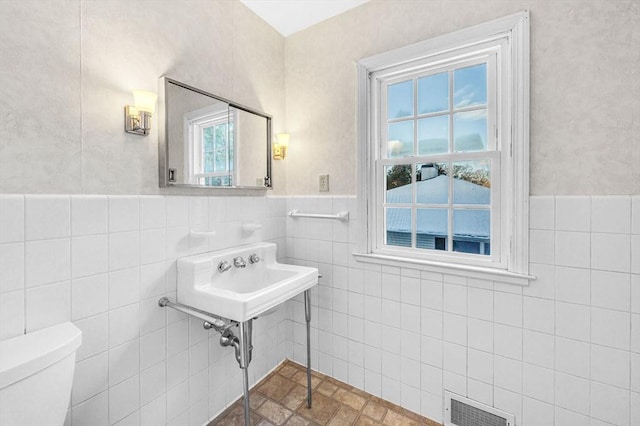 bathroom featuring toilet, a sink, visible vents, tile walls, and wainscoting