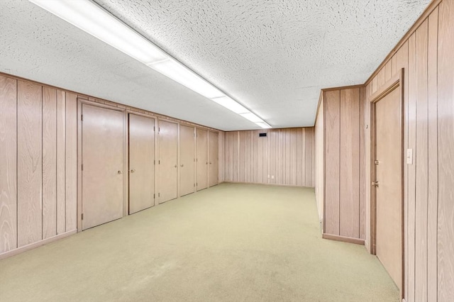 finished basement with a textured ceiling, wood walls, and light colored carpet