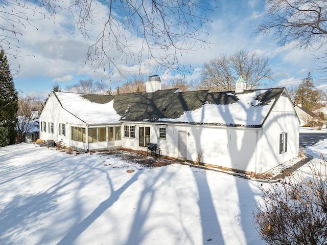 snow covered house with a sunroom and a chimney