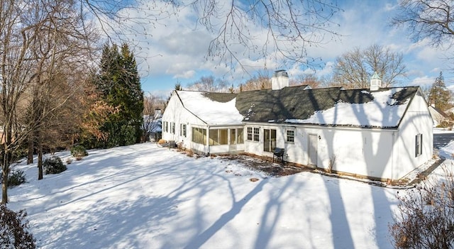 snow covered rear of property featuring a sunroom and a chimney