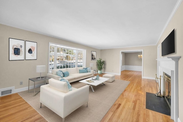 living room with light wood-style floors, visible vents, crown molding, and baseboards