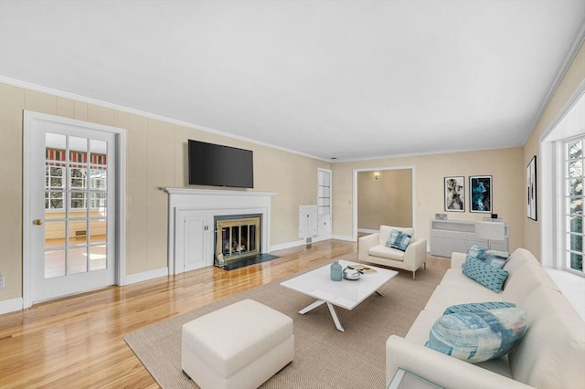 living room with a fireplace with flush hearth, ornamental molding, wood finished floors, and a healthy amount of sunlight