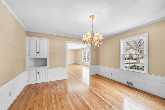 unfurnished dining area with ornamental molding, a wainscoted wall, a notable chandelier, and light wood finished floors