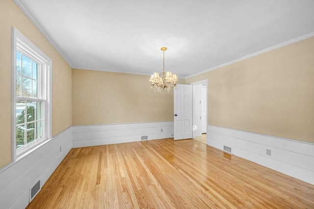 empty room featuring a wainscoted wall, visible vents, a notable chandelier, and wood finished floors