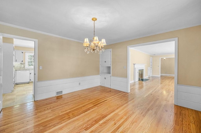 empty room featuring a fireplace with flush hearth, light wood-type flooring, wainscoting, and visible vents