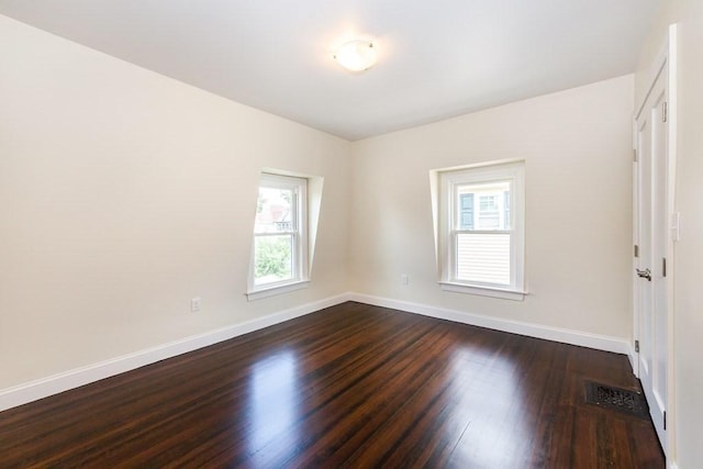 empty room featuring dark wood-style flooring, baseboards, and visible vents