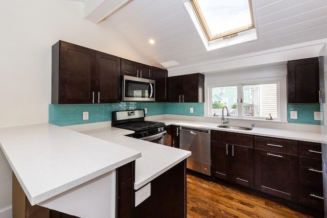 kitchen featuring a peninsula, appliances with stainless steel finishes, light countertops, a sink, and lofted ceiling with skylight