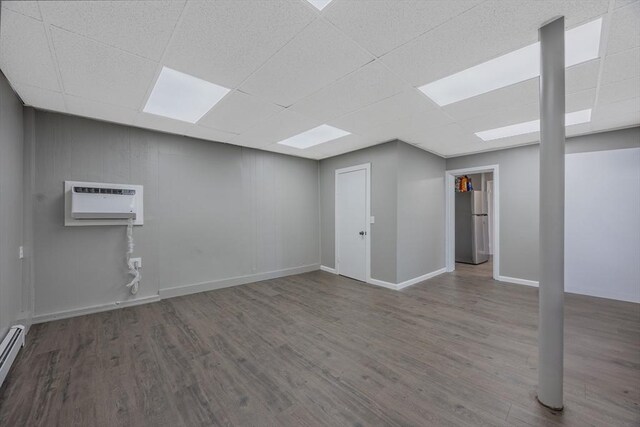 318 Newton St, South Hadley, MA 01075 - below grade area featuring a drop ceiling, wood finished floors, freestanding refrigerator, a baseboard radiator, and an AC wall unit