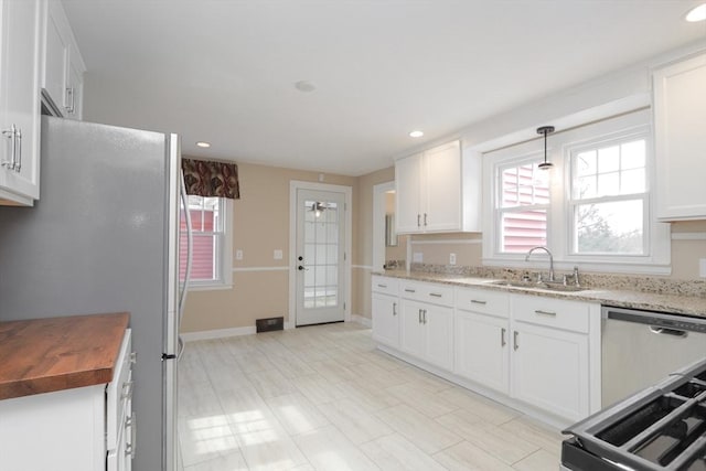 kitchen featuring wooden counters, freestanding refrigerator, a sink, white cabinets, and a wealth of natural light