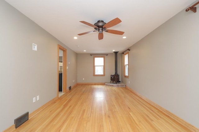 unfurnished room with a wood stove, recessed lighting, light wood-style flooring, and visible vents