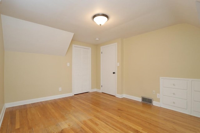 additional living space with light wood-type flooring, visible vents, lofted ceiling, and baseboards